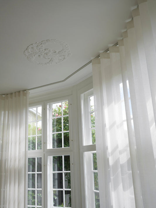 Klassisk hvid 520 gardinskinne i karnap loft monteret med stuk og lette lyse gardiner syet med wavebånd og 8 cm waveglidere